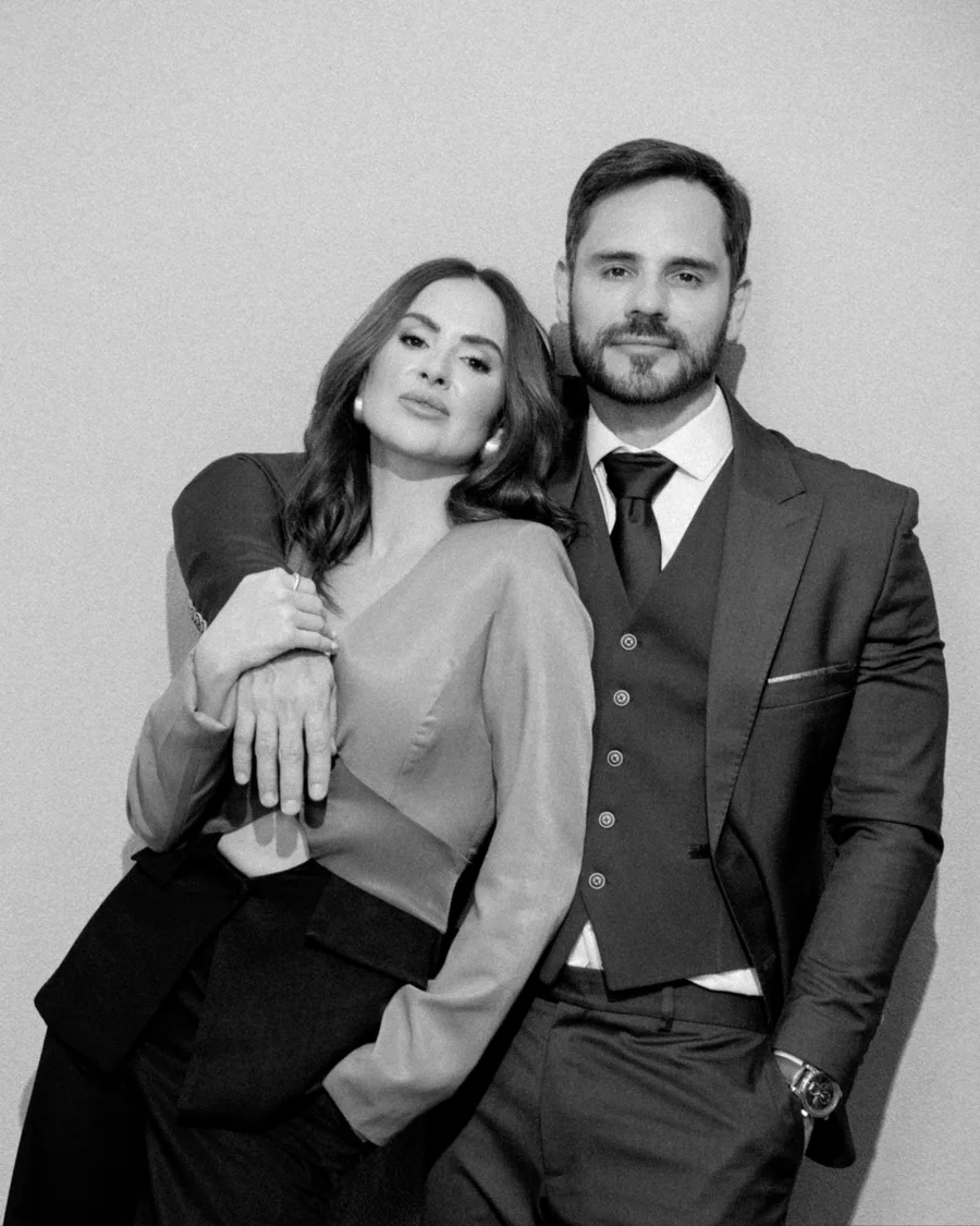 Retrato em preto e branco do casal de médicos da Clínica Senzia, ela com a cabeça apoiada nele, os dois diante de uma parede clara.